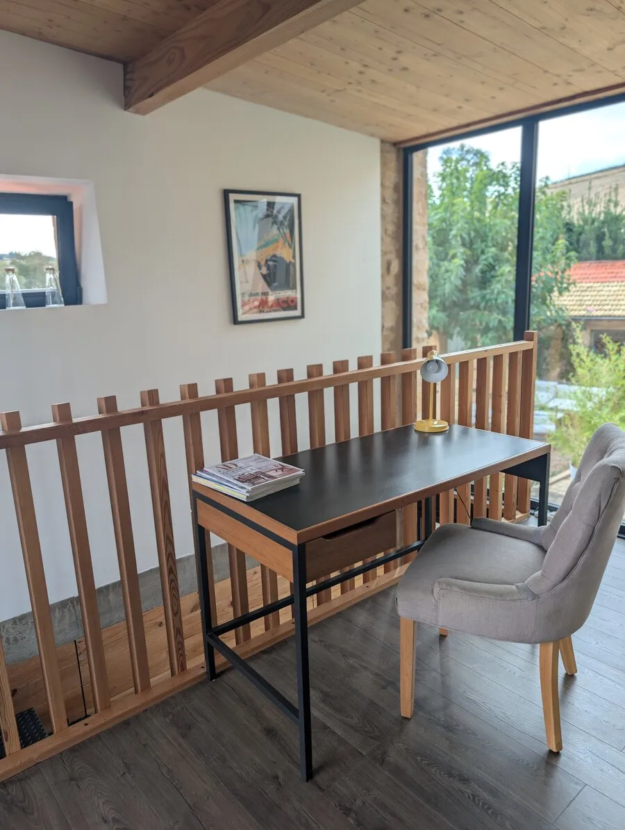 Le bureau et sa chaise, devant la baie vitrée et la balustrade en bois