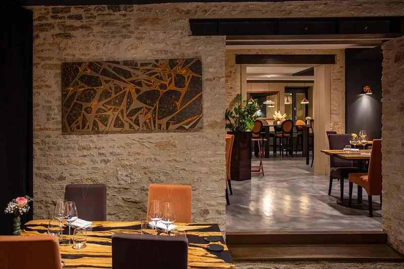 La salle de Cassis, un mur en pierre orné d’un grand panneau doré et les tables dressées