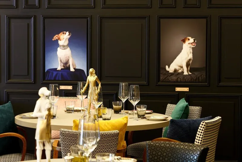 Une table ronde dressée sous deux portraits de chiens, chez Lucienne fait des siennes