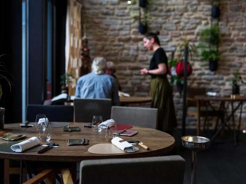 La salle d’Aux Terrasses, une table ronde dressée au premier plan et un mur en pierre couvert de plantes